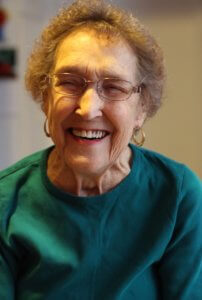 Headshot of white elderly woman smiling and squinting her eyes.