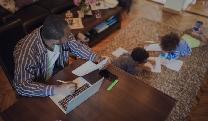 father on laptop while children on the rug drawing