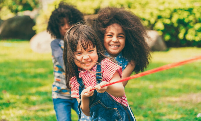 Happy children playing tug of war and having fun during summer camping in the park. Children recreation concept.