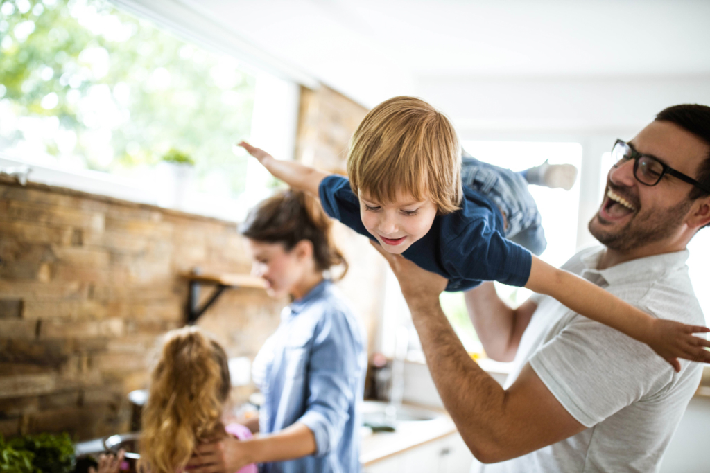 Happy little boy having fun with his father at home. There are people in the background.