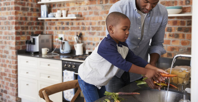 Son Helping Father To Prepare Vegetables For Meal In Kitchen