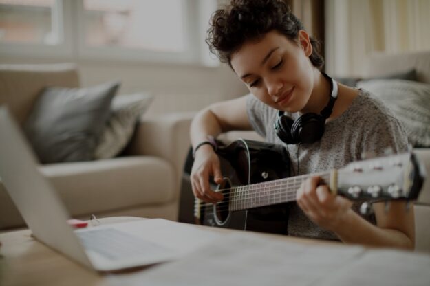 learner playing guitar in front of a laptop