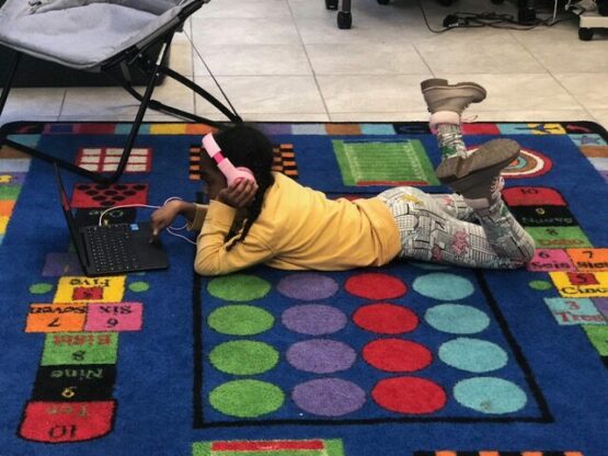 photo of a young learning lying on a rug looking at a laptop