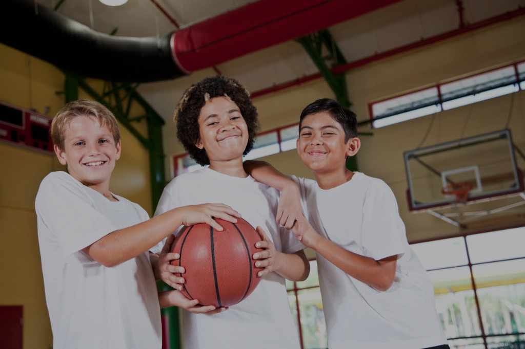 young learners taking a group photo in a gym holding a basketball