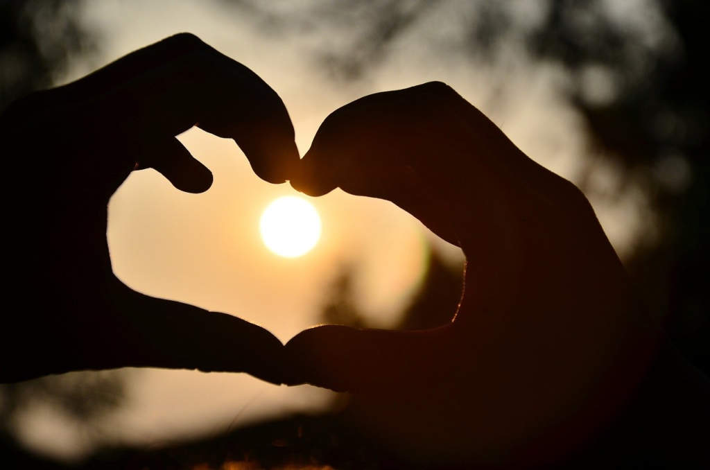 close up of hands making a heart in front of the sun