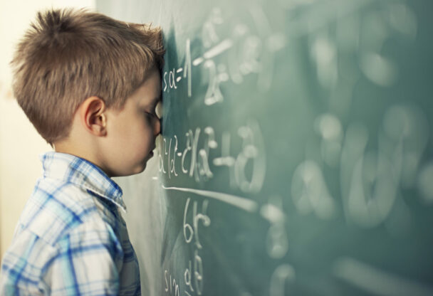 photo of a young learner with his head against a chalkboard