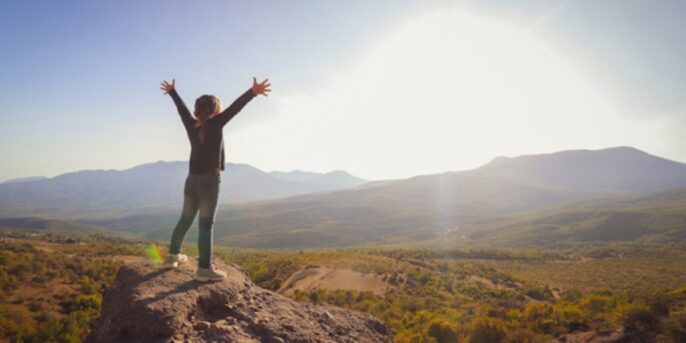 person looking out to mountains with their arms out